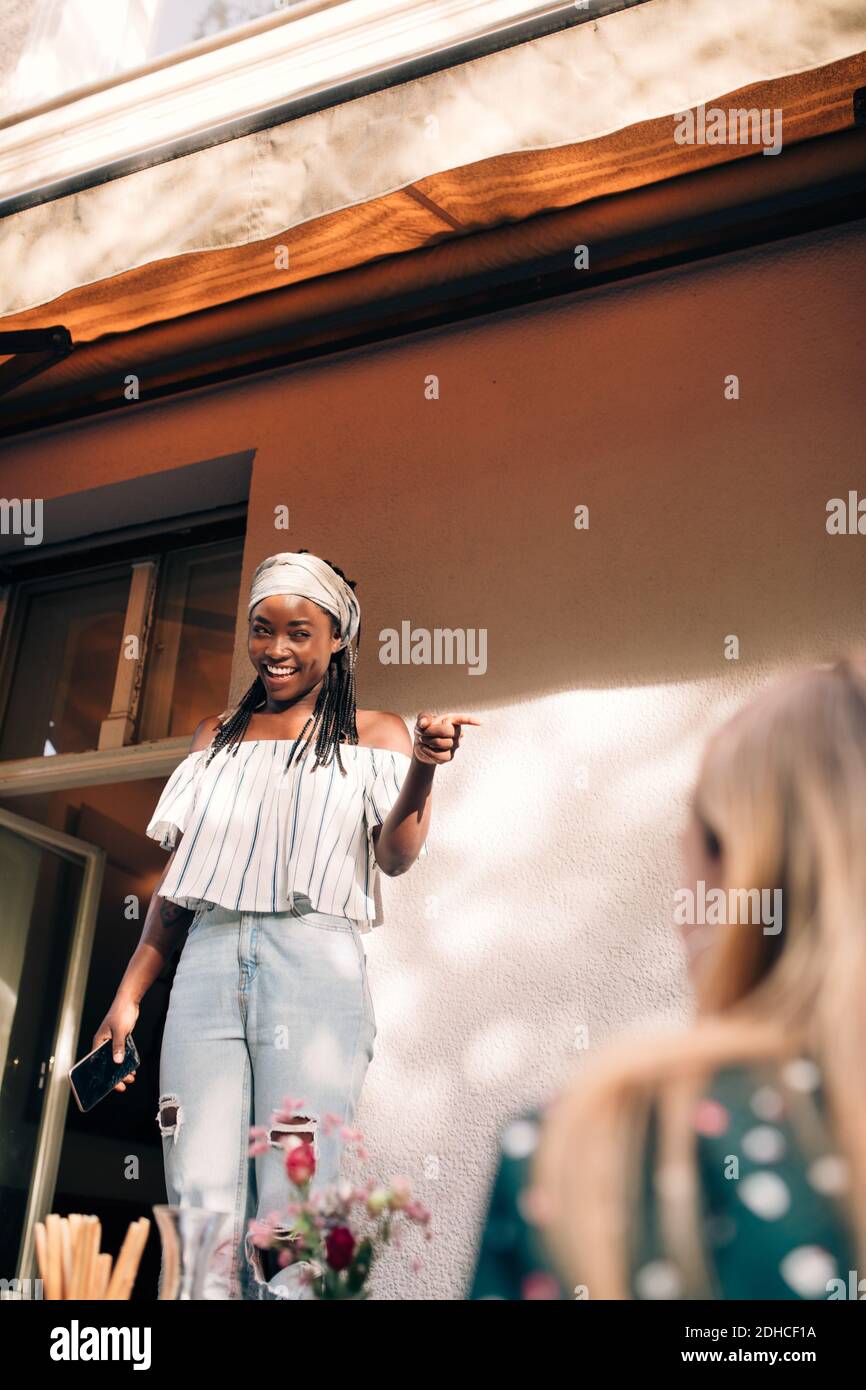 Smiling young woman pointing while standing in balcony Stock Photo