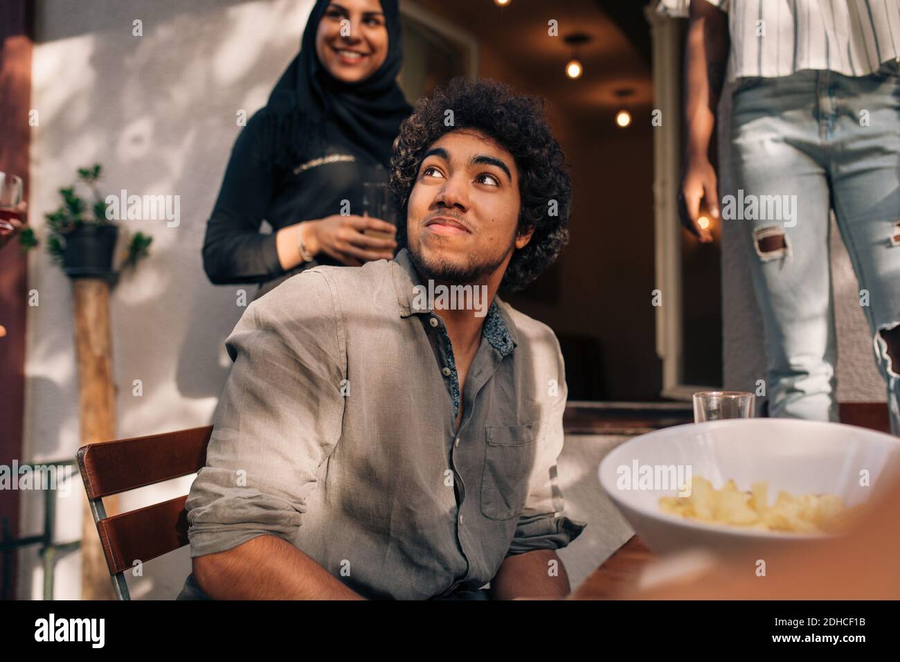 Young man looking up while sitting at table in balcony Stock Photo