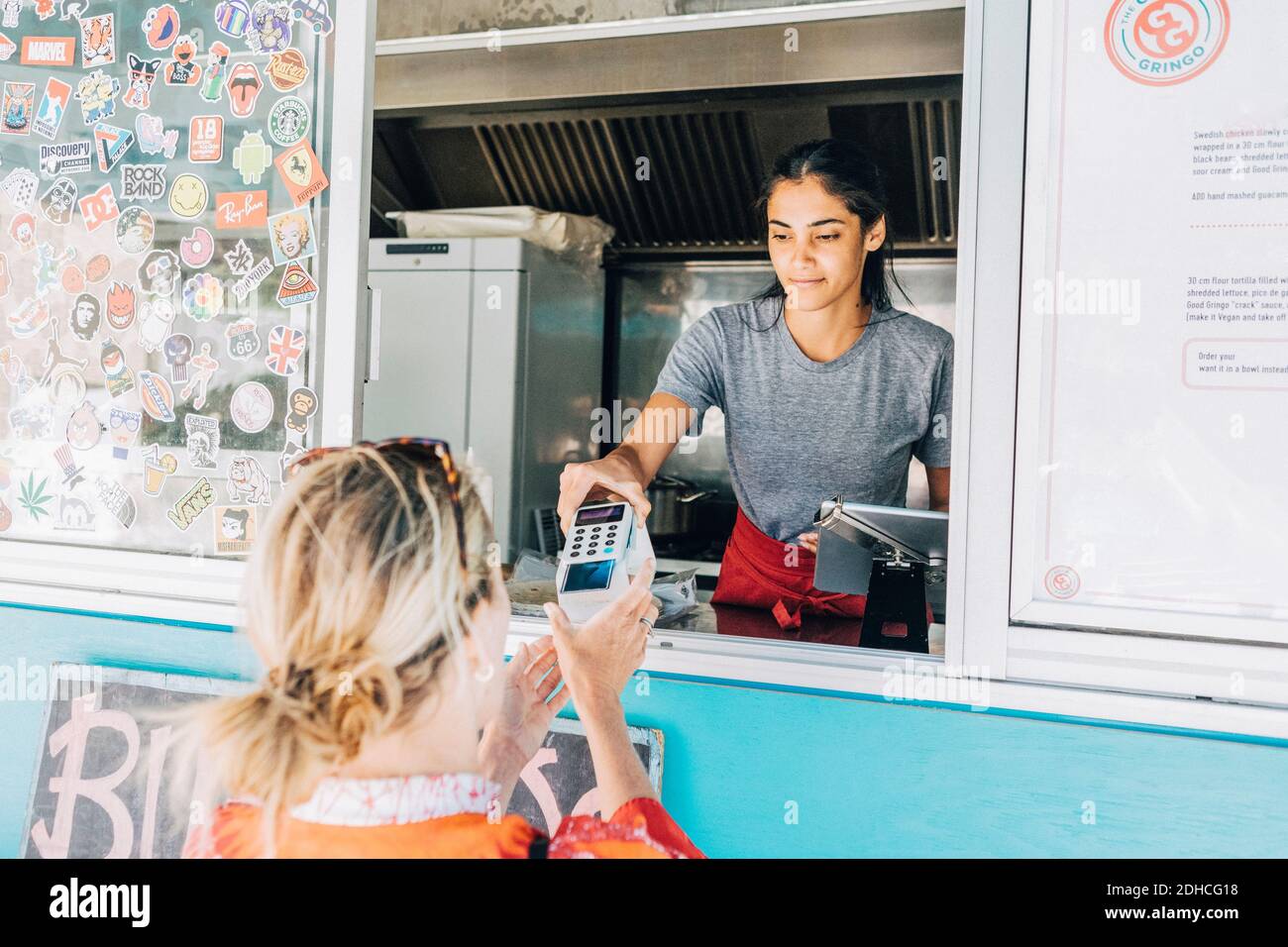 Young female owner standing giving credit card reader to blond customer