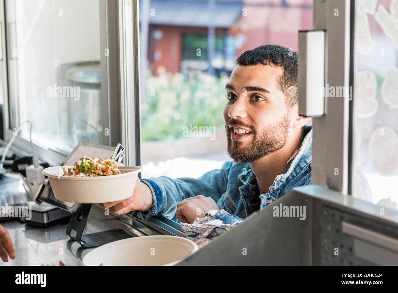 Smiling young male customer holding fresh Tex-Mex in bowl at concession stand Stock Photo