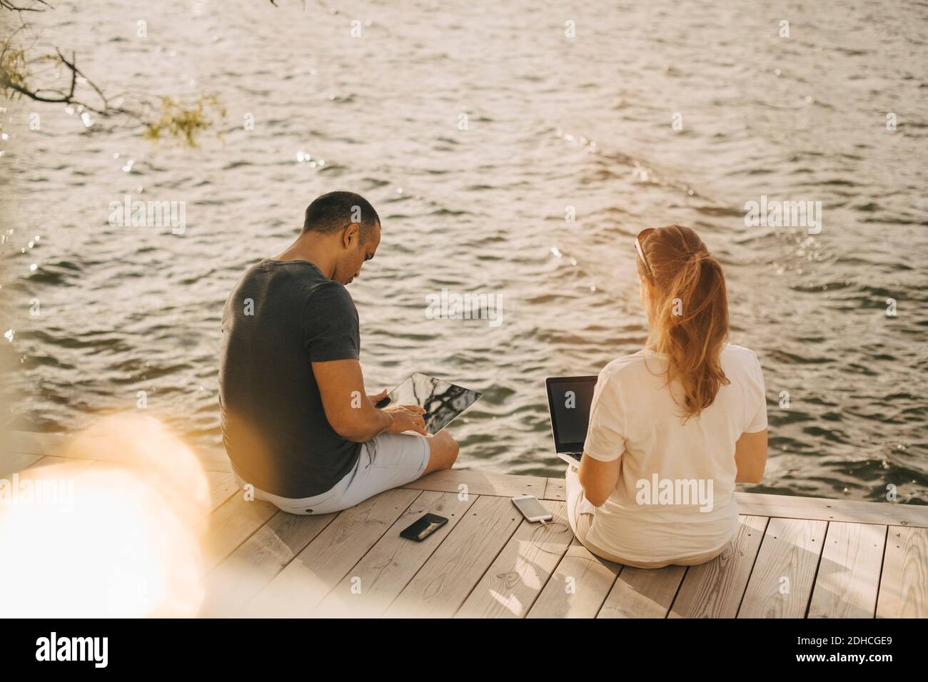 Mature couple using laptop while sitting on patio against lake during ...
