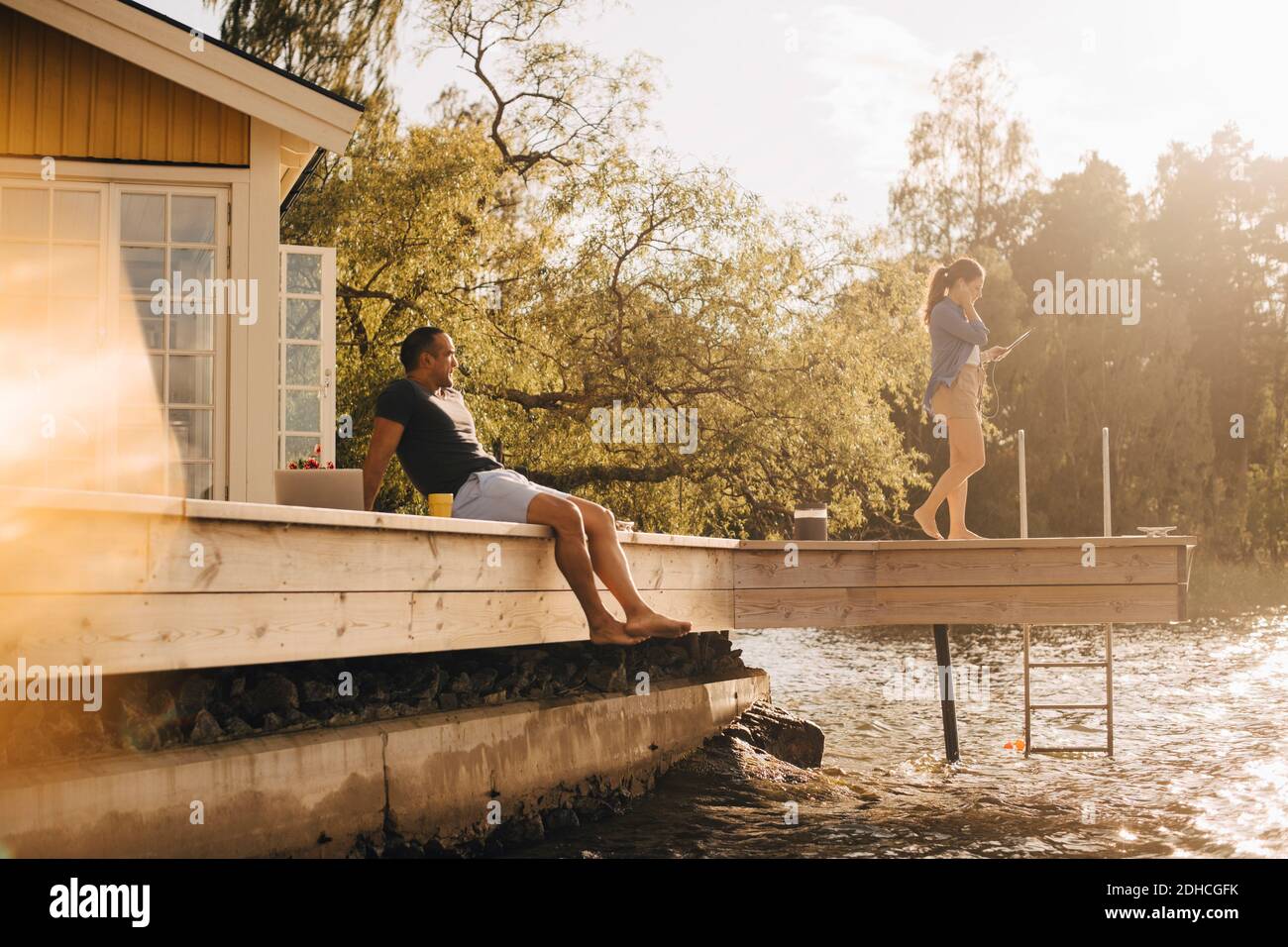 Mature man looking at woman using digital tablet while sitting on patio by lake Stock Photo