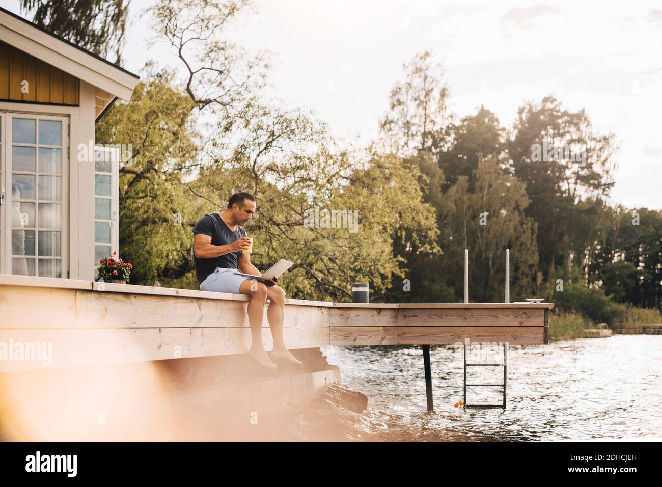 Mature man having juice while using laptop on patio by lake Stock Photo