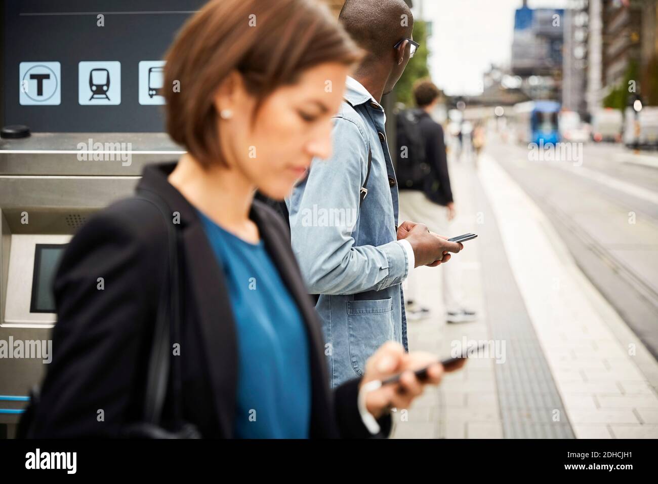Commuters using smart phone while waiting on sidewalk in city Stock Photo