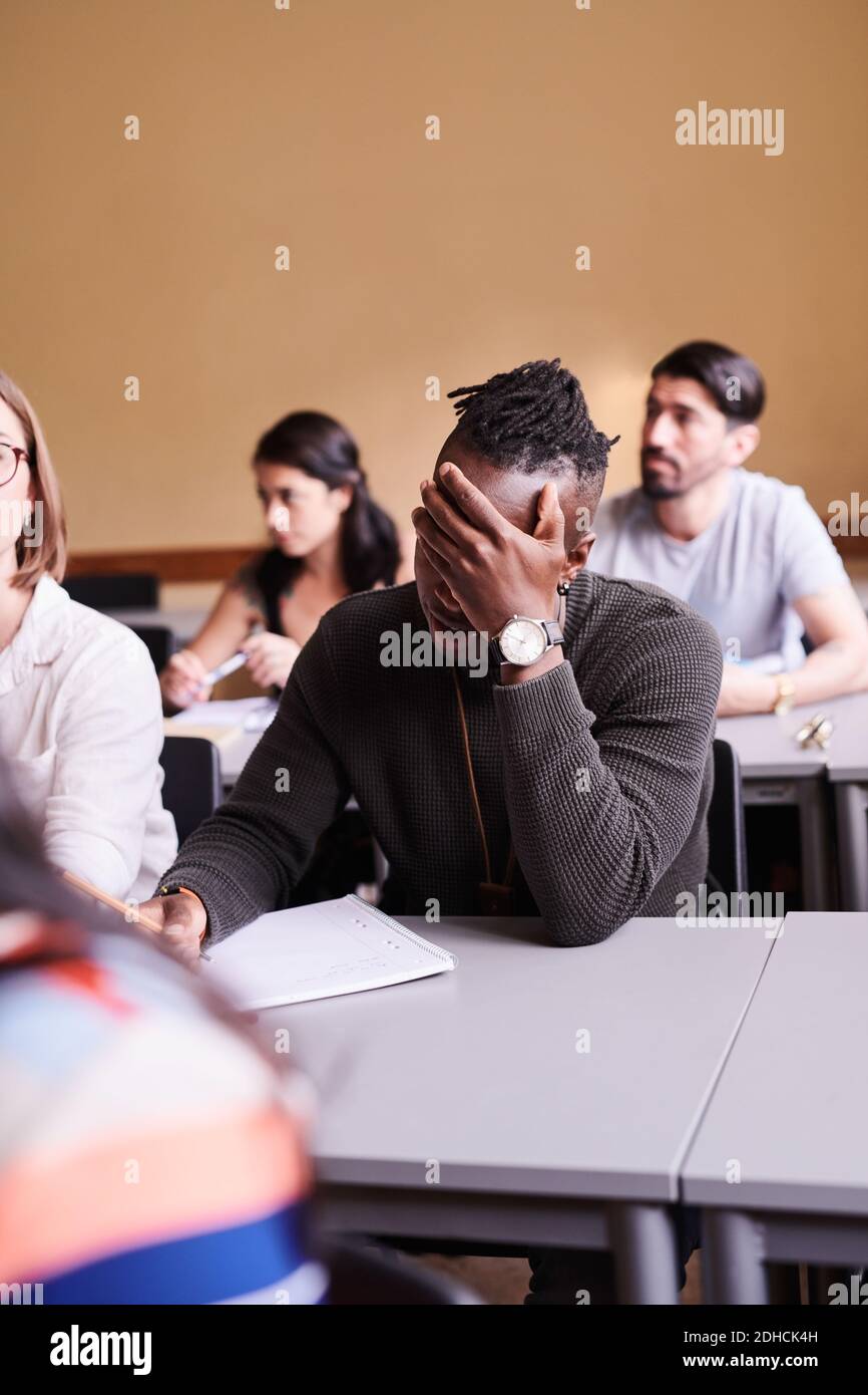 Bored young man writing while sitting at desk in language school Stock Photo