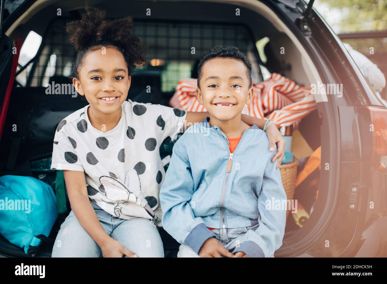 Portrait of smiling girl sitting with arm around on brother in electric car trunk Stock Photo