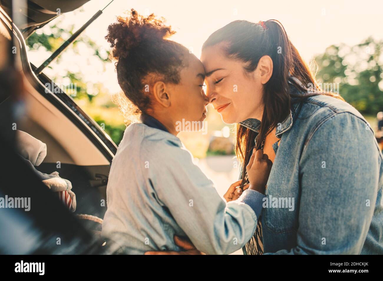 Smiling woman and daughter sitting face to face with eyes closed in car trunk during picnic Stock Photo