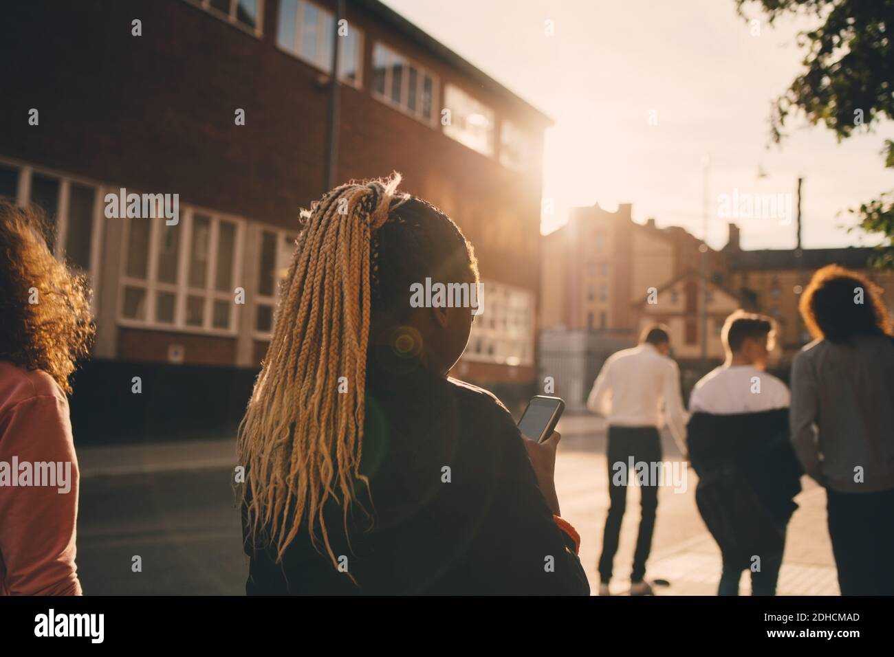 Rear view of teenage girl text messaging on smart phone while walking with friends in city Stock Photo