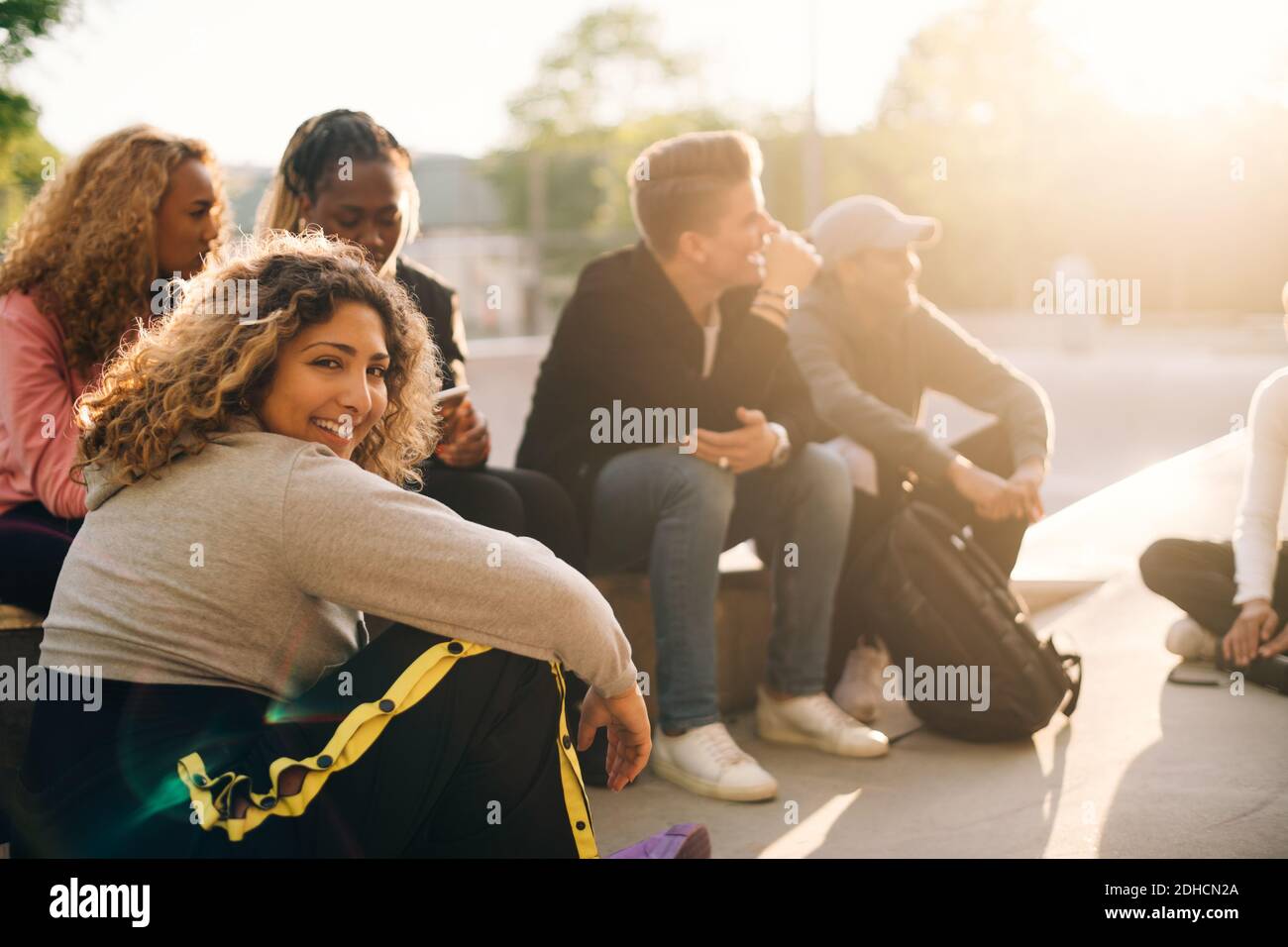 Portrait of smiling young woman sitting with friends at skateboard park Stock Photo