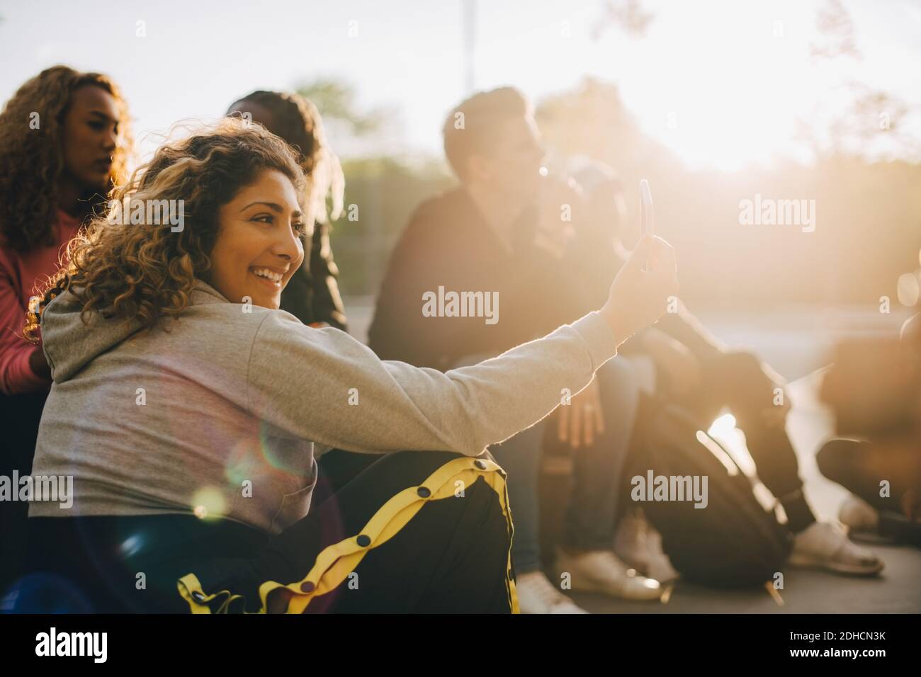 Happy woman taking selfie on smart phone while sitting with friends at park Stock Photo