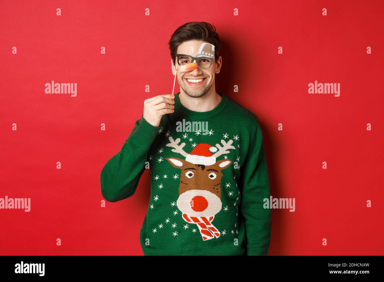 Funny man in christmas sweater and party mask, celebrating winter holidays,  smiling happy, standing over red background Stock Photo - Alamy