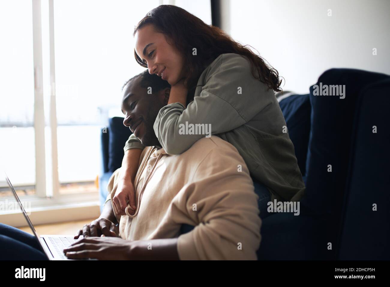 Woman hugging man from behind as young mixed ethnicity couple relax on ...