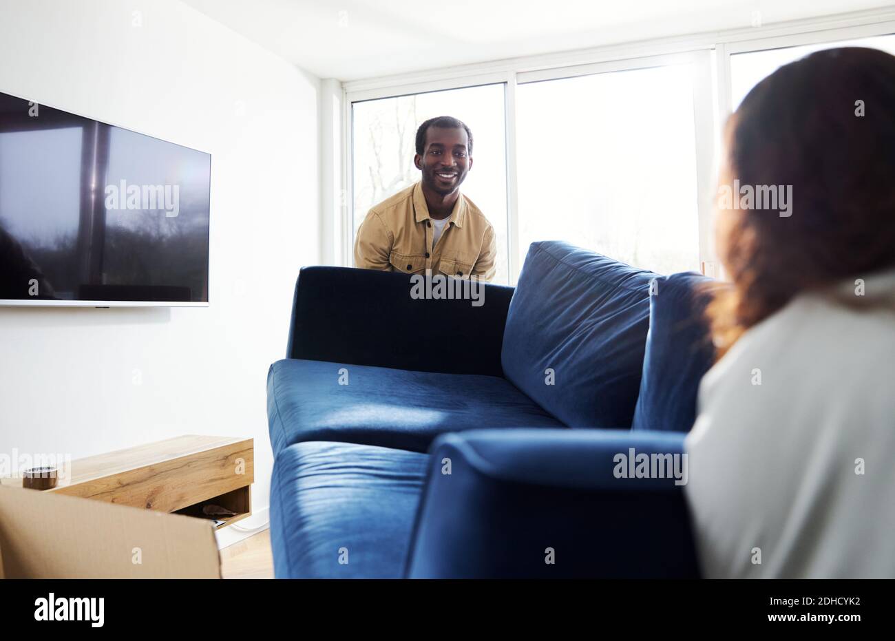 Young mixed ethnicity couple on moving day into new home carrying sofa in lounge surrounded by removal boxes together Stock Photo