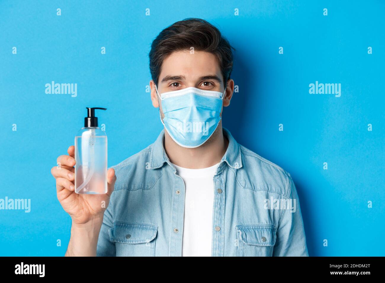 Concept of coronavirus, pandemic and preventive measures. Close-up of young man in medical mask advice to use hand sanitizer, sh Stock Photo
