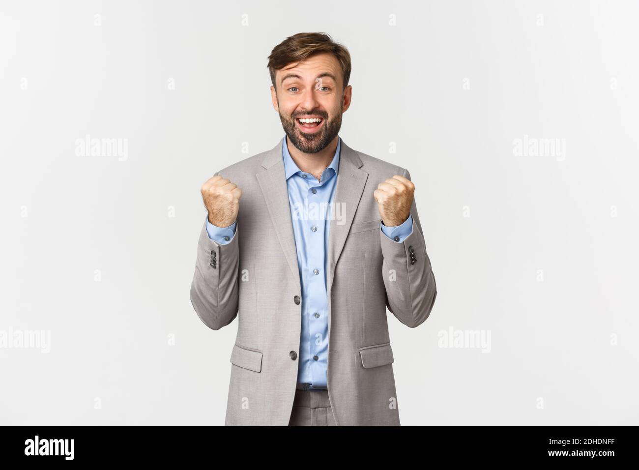 Portrait of relieved and happy businessman with beard, wearing grey suit, achieve goal, clenching fists like a winner, triumphin Stock Photo