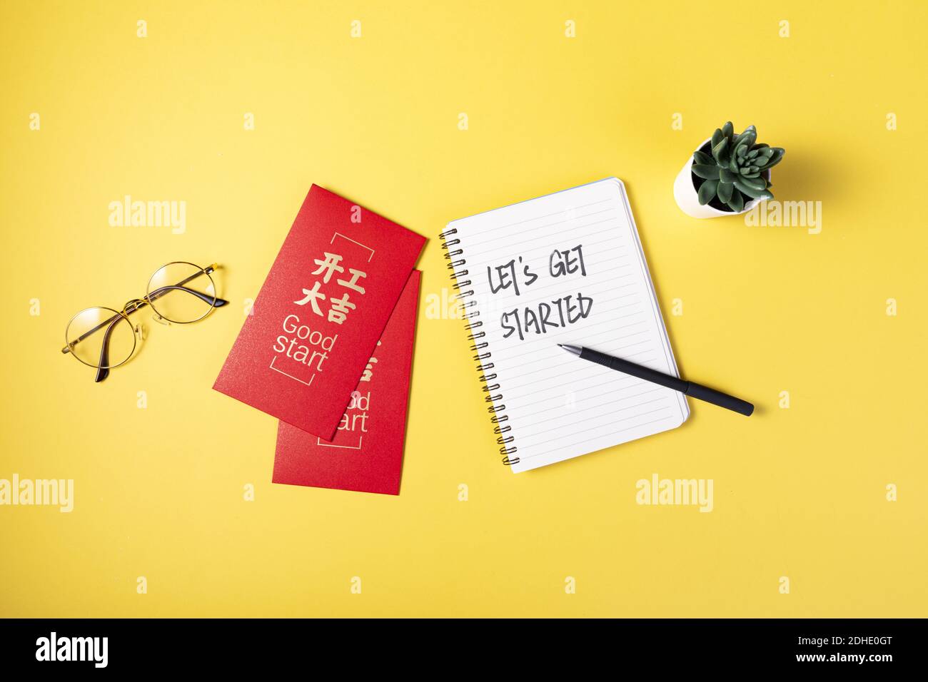 A notebook with "LET'S GET STARTED" text and good start red envelopes on yellow background Stock Photo