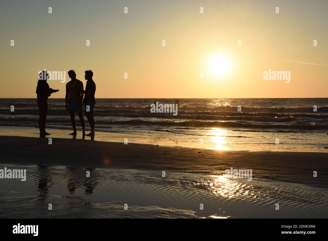 Silhouette of three people standing on Clearwater beach talking at sunset. Stock Photo