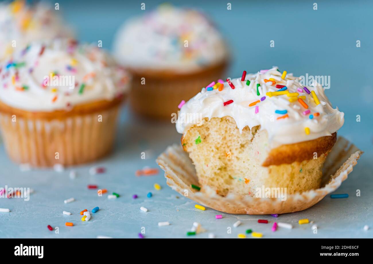 Close up of a half eaten cupcake with white frosting and sprinkles