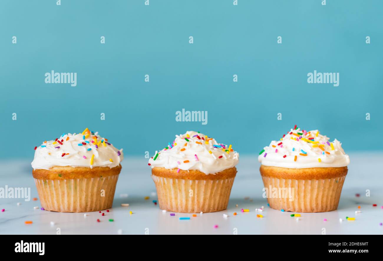 Cupcakes with sprinkles on white table with blue background. Stock Photo