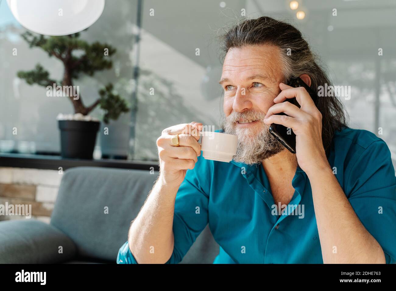 Mature man with beard talking on the phone and drinking coffee sitting Stock Photo