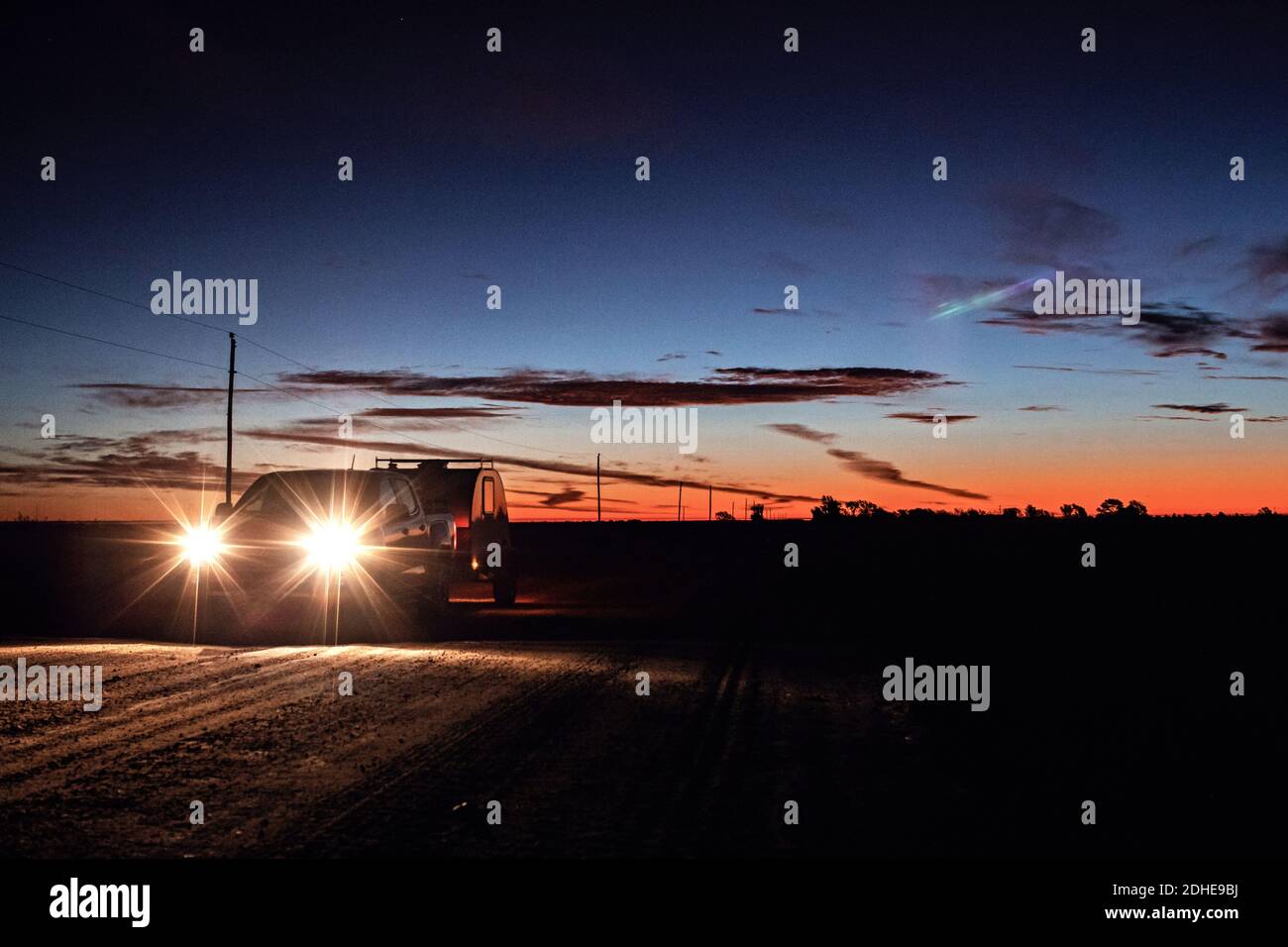 Pickup truck towing teardrop camper with bright headlights sunrise Stock Photo