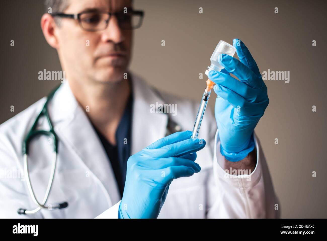 Doctor in white coat drawing vaccine into a syringe for injection. Stock Photo