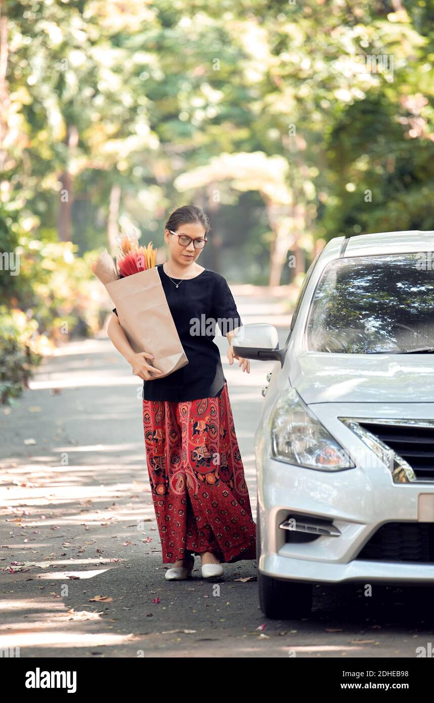 A woman hold a paper bag of dry flower and back to car after shopping Stock Photo