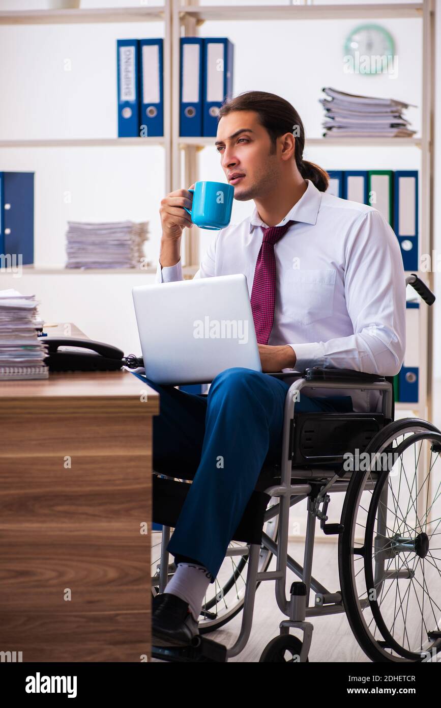 Young male employee after accident in wheel-chair at workplace Stock Photo
