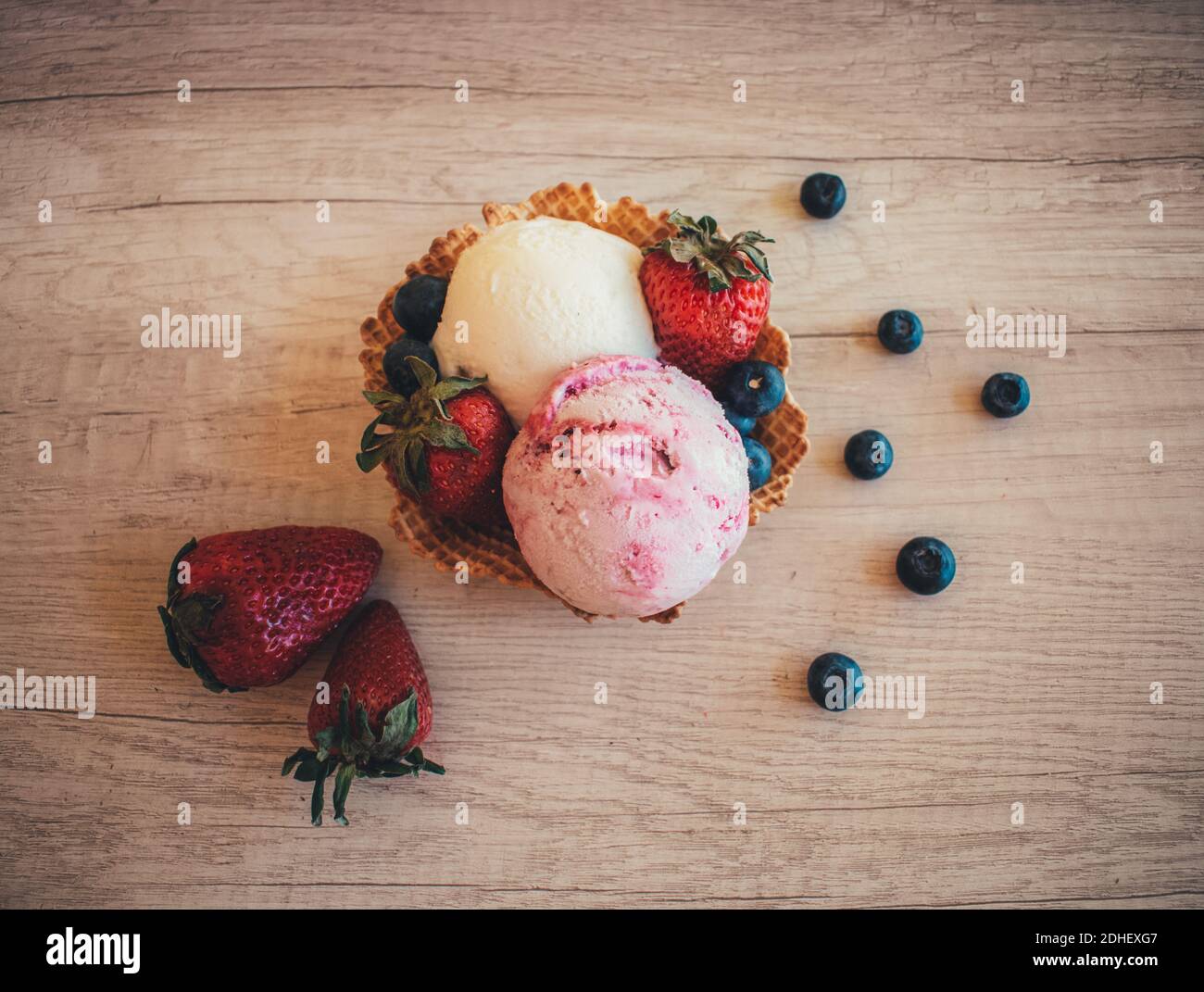 A top view of two scoops of strawberry and vanilla ice cream in a waffle cone on a wooden surface Stock Photo