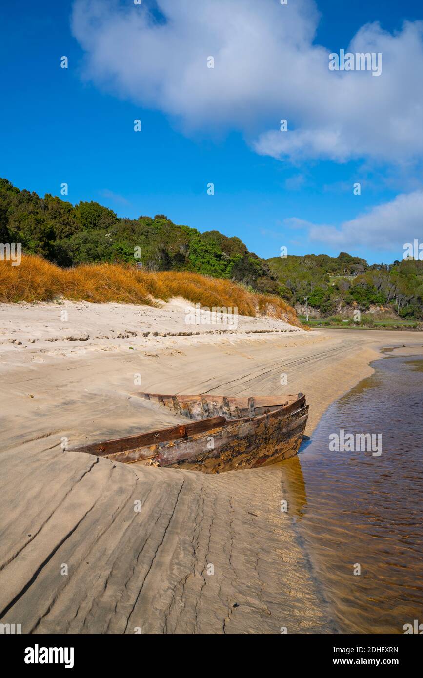 Lines and patterns curving along edge of Mill Creek interupted by bow of old wooden boat  stuck in sand  at beach on Stewart Island. Stock Photo