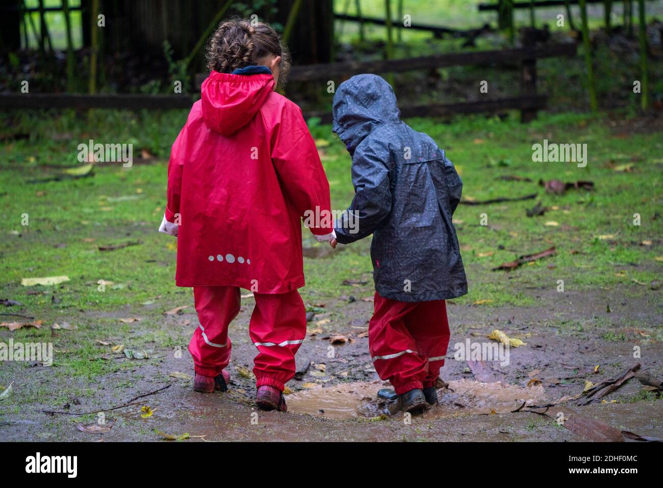 Two young kids having fun playing outside in the mud while wearing coloful raincoats Stock Photo