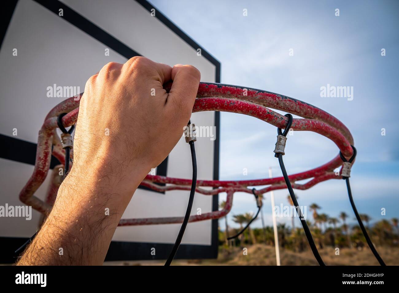 The player's hand holding the basketball hoop on the beach under a
