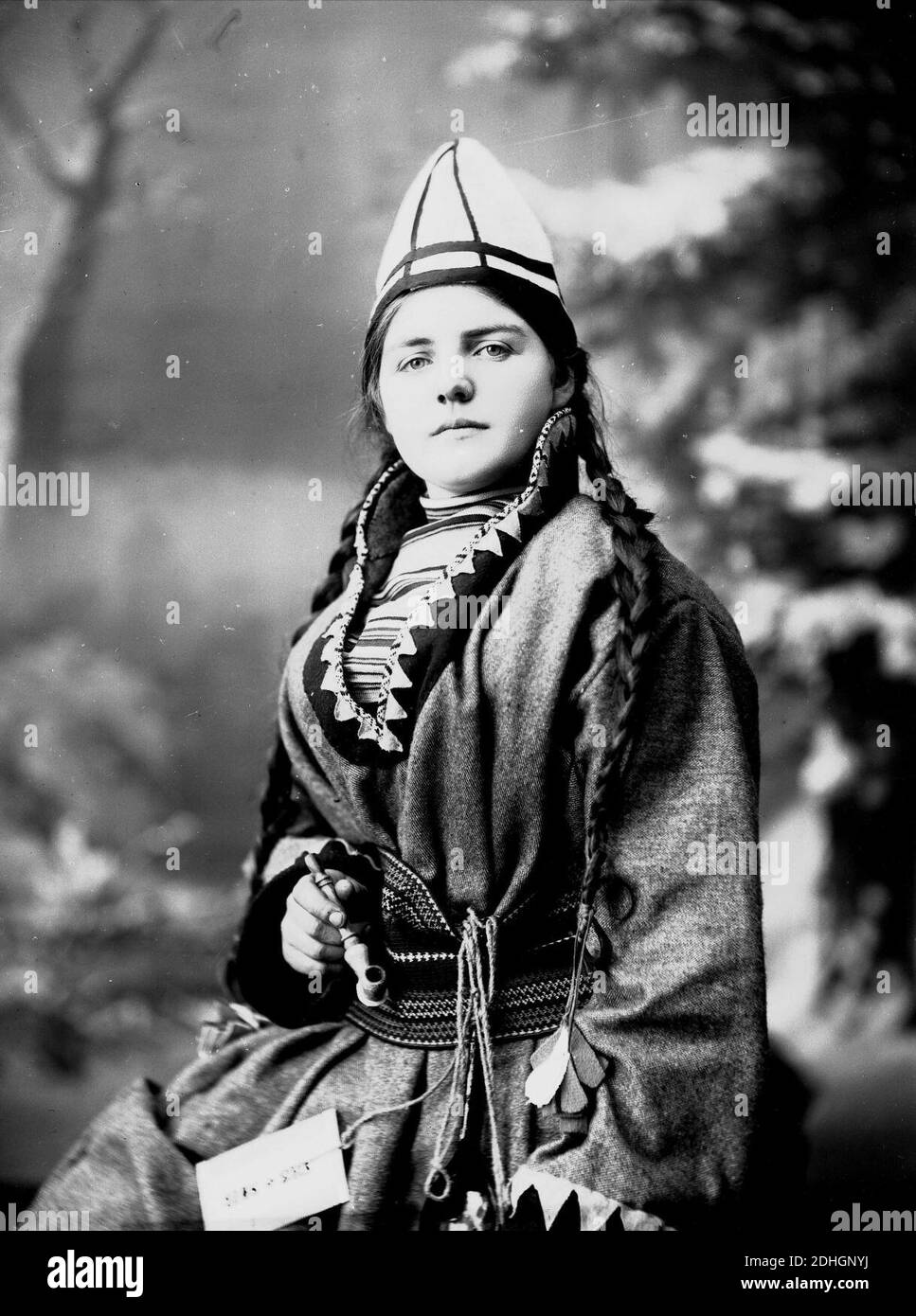 Kvinne i samisk drakt, kofte, lue og nålehus med beltering. I den ene hånden holder hun en pipe Stock Photo