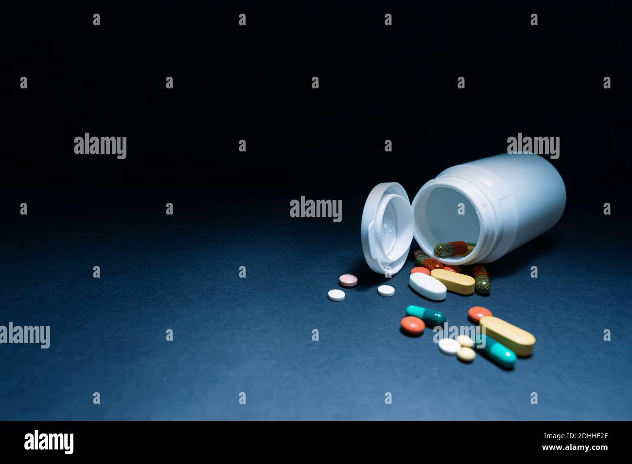 Medical bottles and medication pills spilling out on to pastel blue