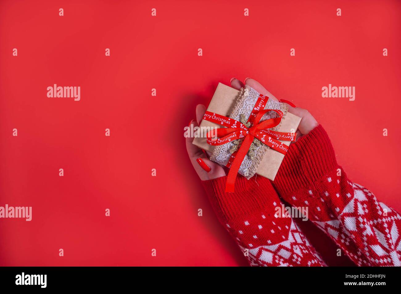 Top view of female hands holding present box package in the palms isolated over flat lay red background.  Christmas background with copy space. Stock Photo