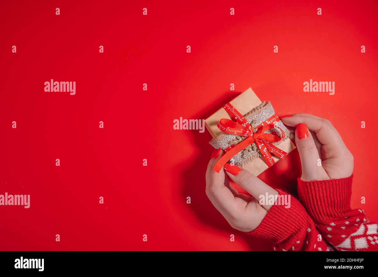 Top view of female hands holding present box package in the palms isolated over flat lay red background.  Christmas background with copy space. Stock Photo
