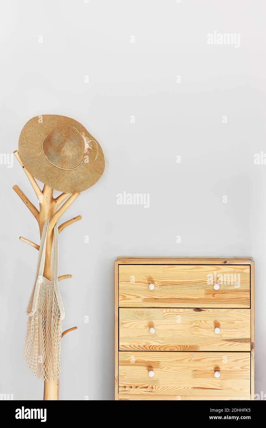 Minimalistic hallway interior with trendy wooden clothes hanger stand and commode against a gray wall.Wicker hat and mesh bag on the hanger.Copy space Stock Photo