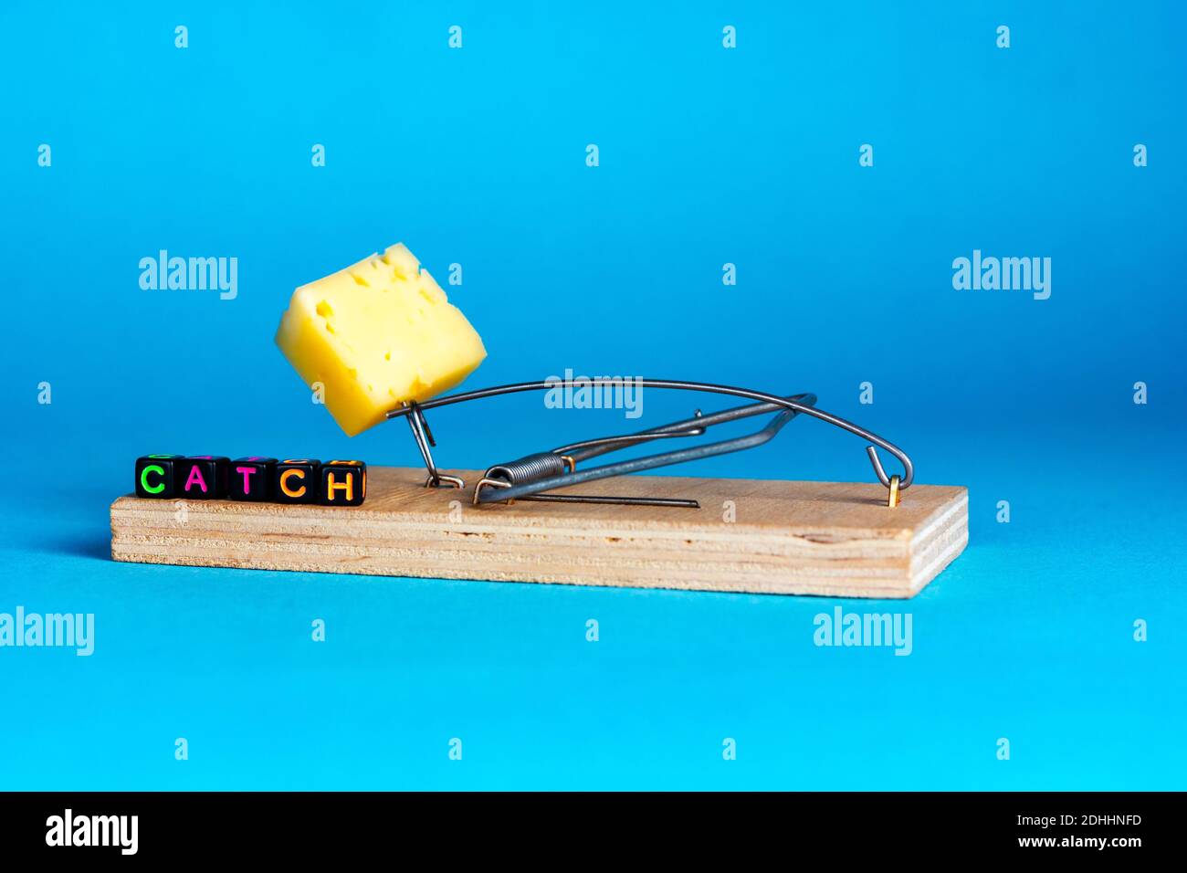 Wooden mousetrap with a piece of cheese and the inscription catch on a blue background Stock Photo