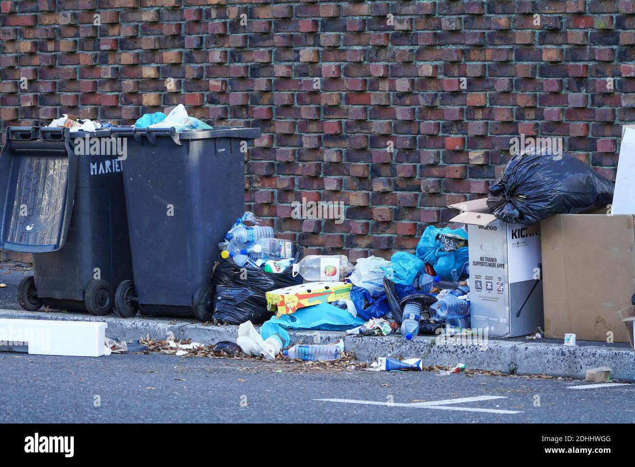 litter next to a bin, garbage bins overflowing onto the pavement with