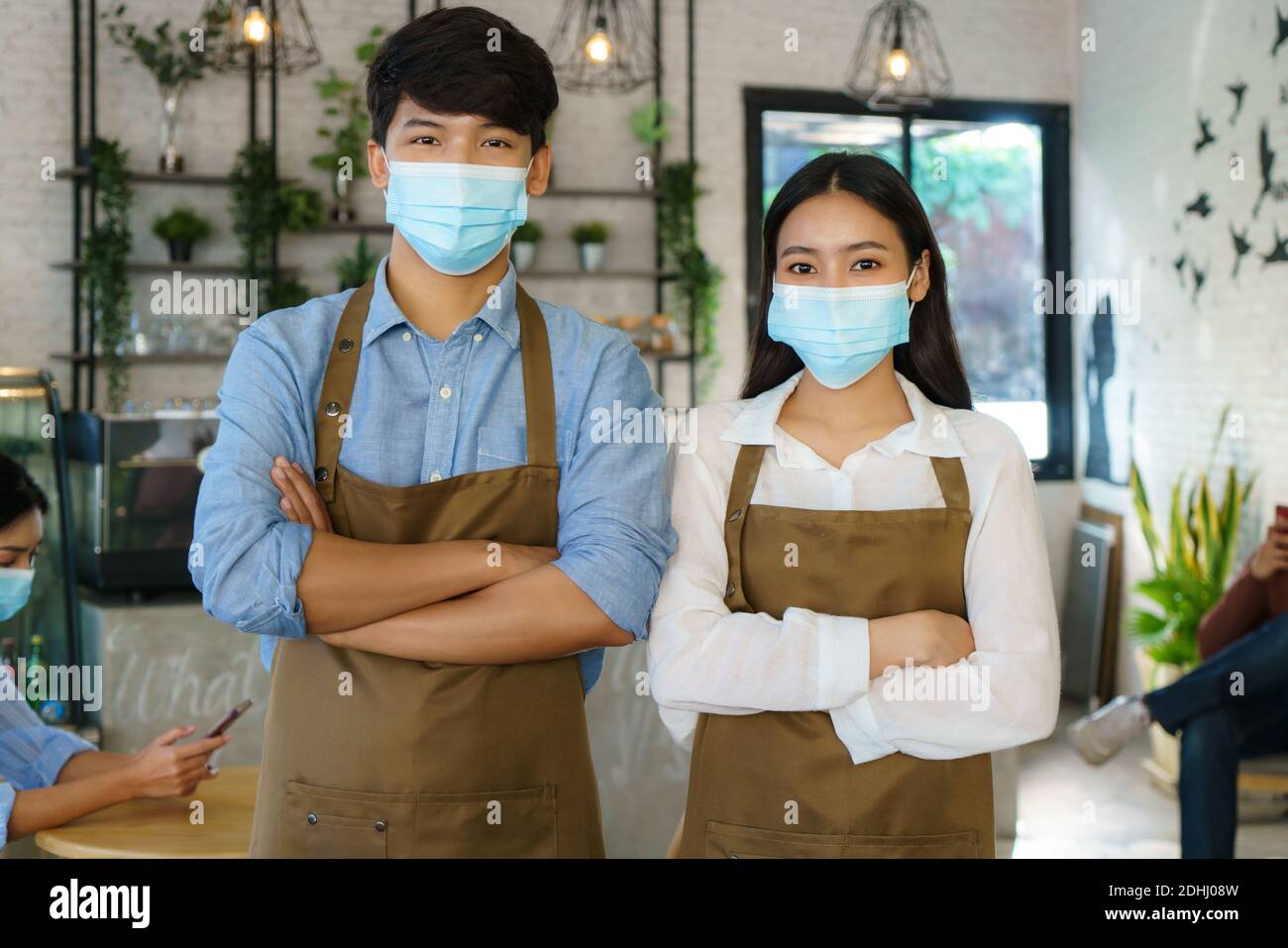 Asian Barista couple in apron and face mask looking at camera ready to give Coffee Service at the modern coffee shop Stock Photo