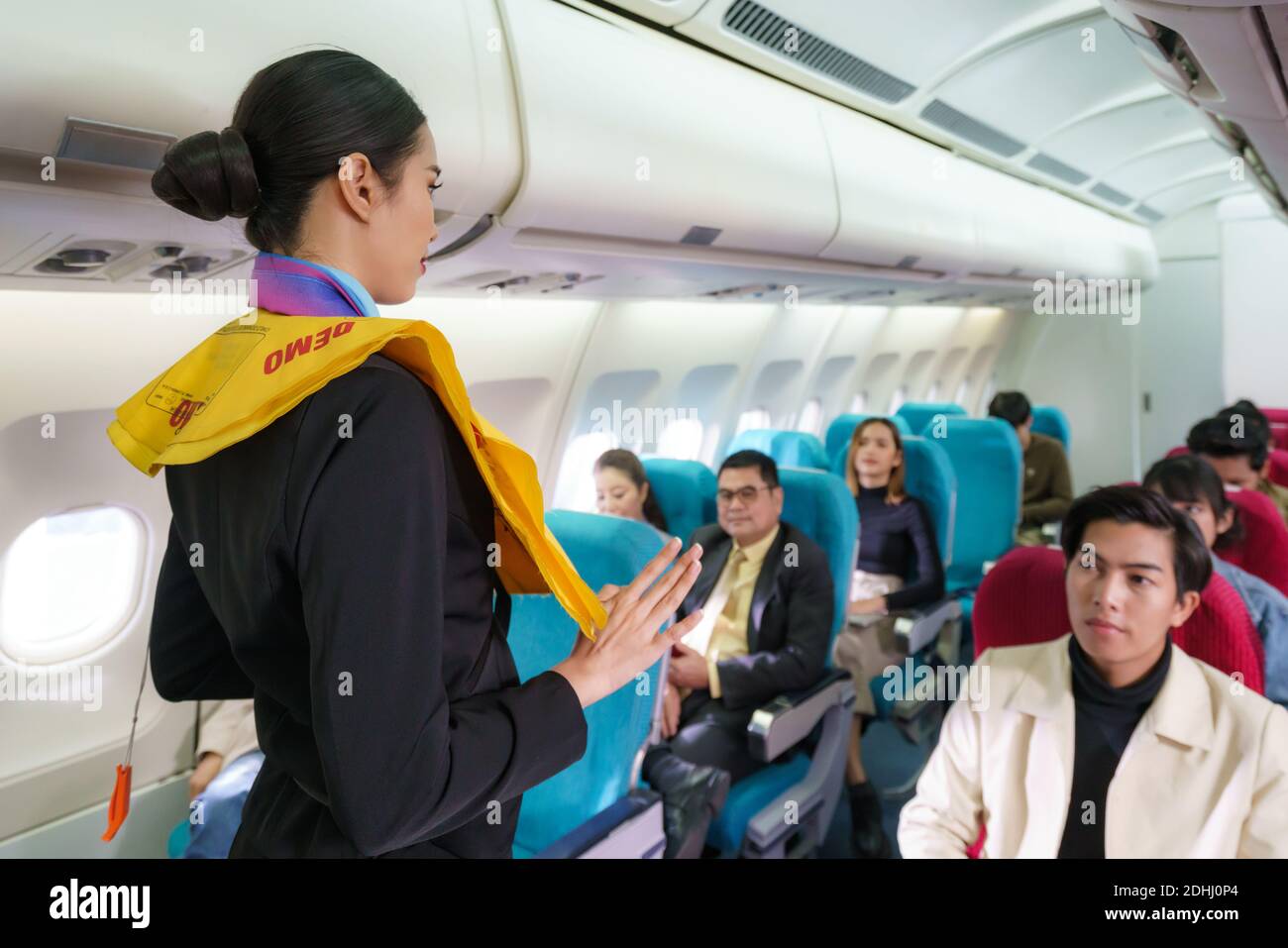 Asian Air hostess staff airline demonstrate safety procedures to passengers prior to flight take off in cabin airplane. Stock Photo