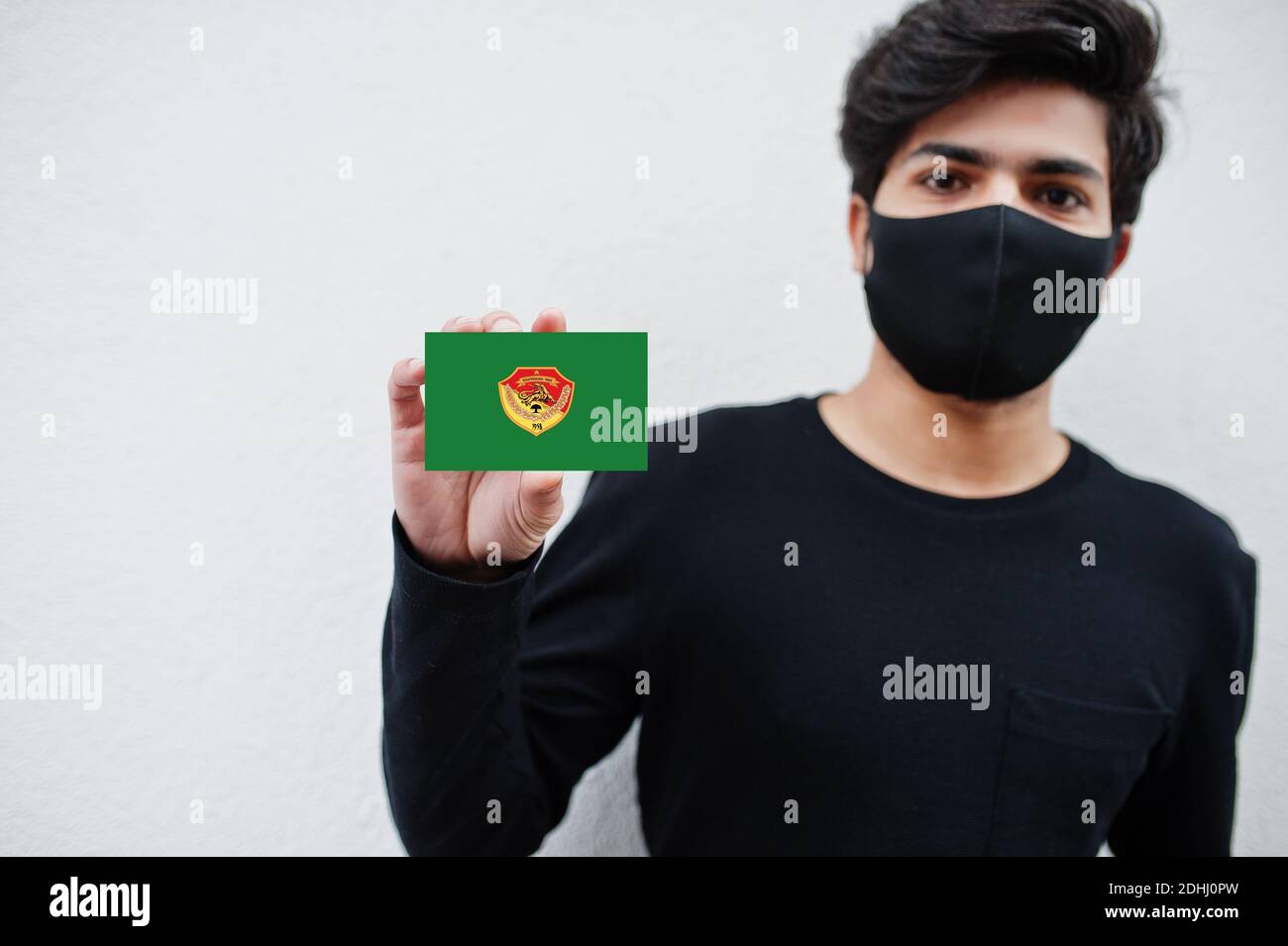 Indonesian man wear all black with face mask hold East Nusa Tenggara flag in hand isolated on white background. Provinces of Indonesia coronavirus con Stock Photo