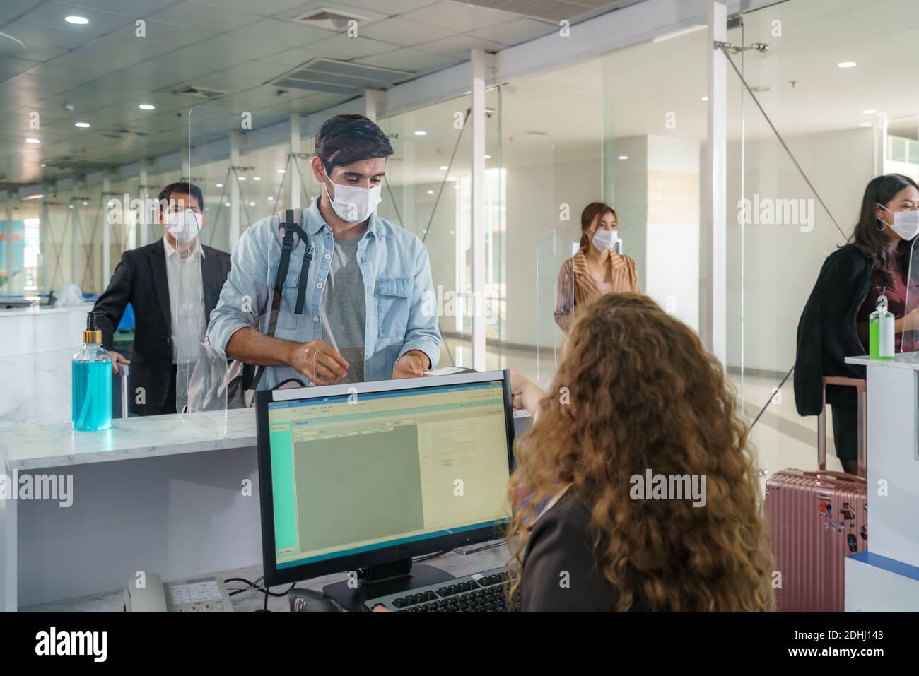 A male airline passengerwith mask is handing over his passport at the airline counter check in through an acrylic barrier for disease prevention coron Stock Photo
