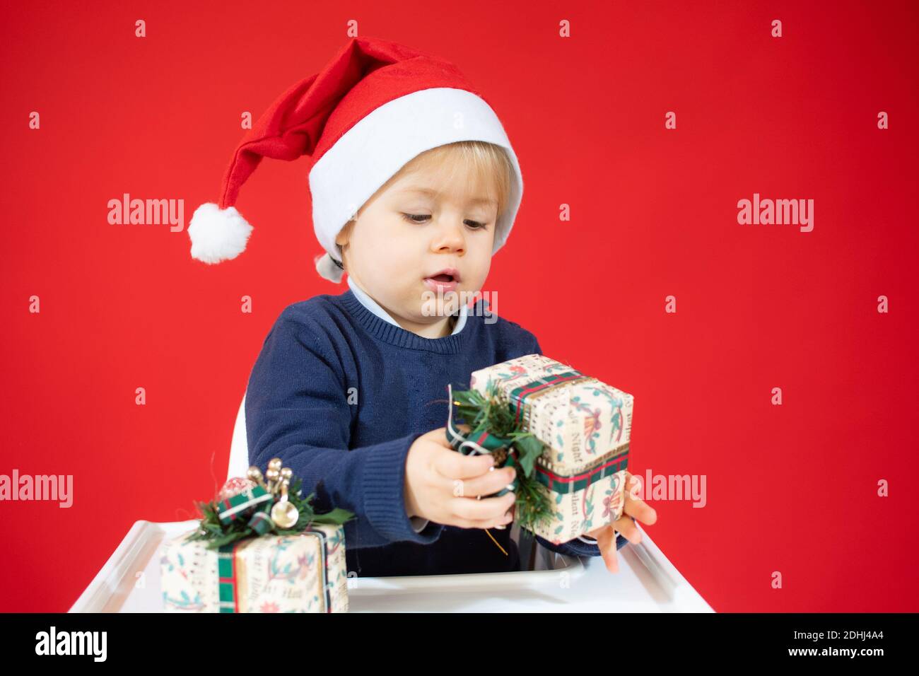 Adorable christmas child in santa hat sitting isolated over red ...