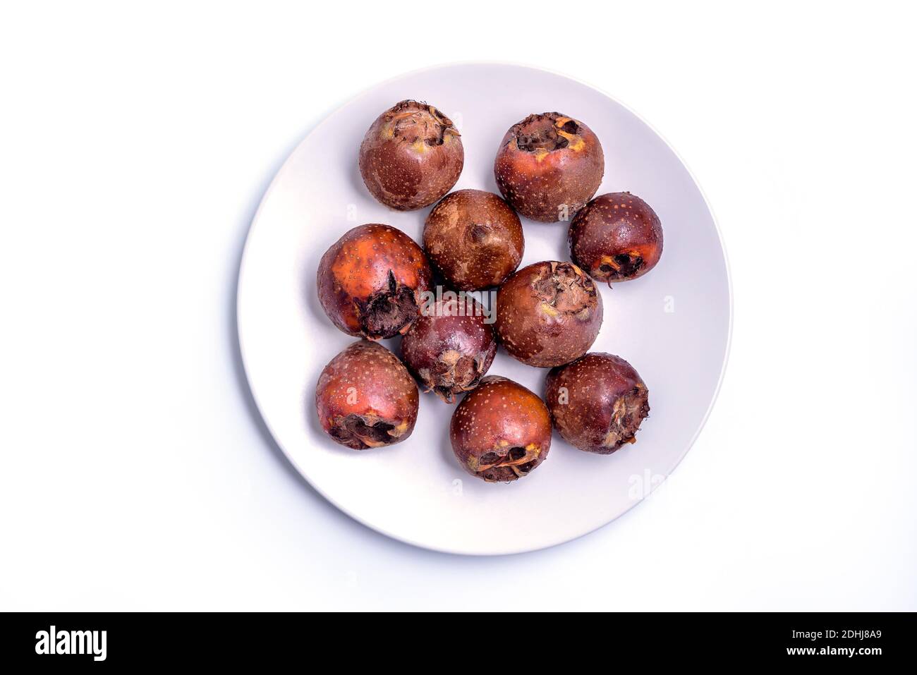 Fresh ripe organic common medlar fruit on a plate on white background. Healthy food Mespilus germanica, top view Stock Photo