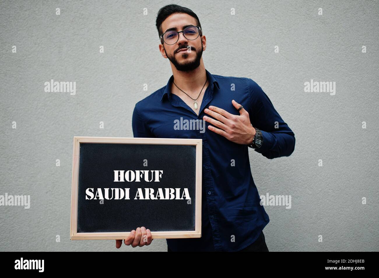 Arab man wear blue shirt and eyeglasses hold board with Hofuf  Saudi Arabia inscription. Largest cities in islamic world concept. Stock Photo