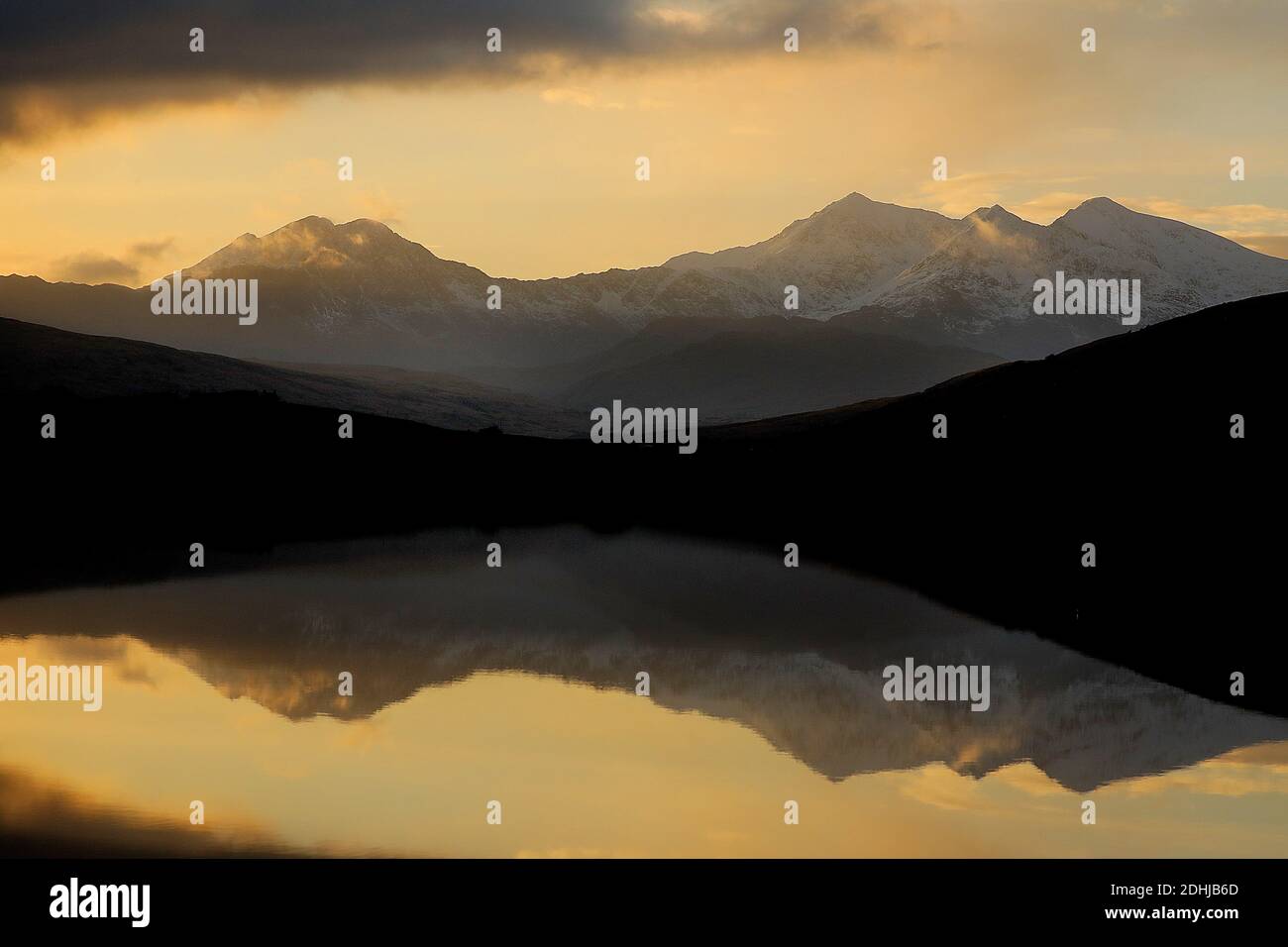 Sunset over the Snowdon horseshoe across showing recent snowfall beyond a flat calm Llynnau Mymbyr. Wales. Picture taken 5th December 2020 Stock Photo
