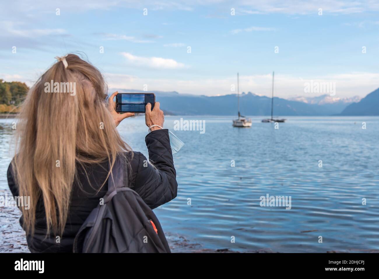 Woman taking a photo at Lake Geneva. She is holding a surgical mask. Concept of new normality Stock Photo