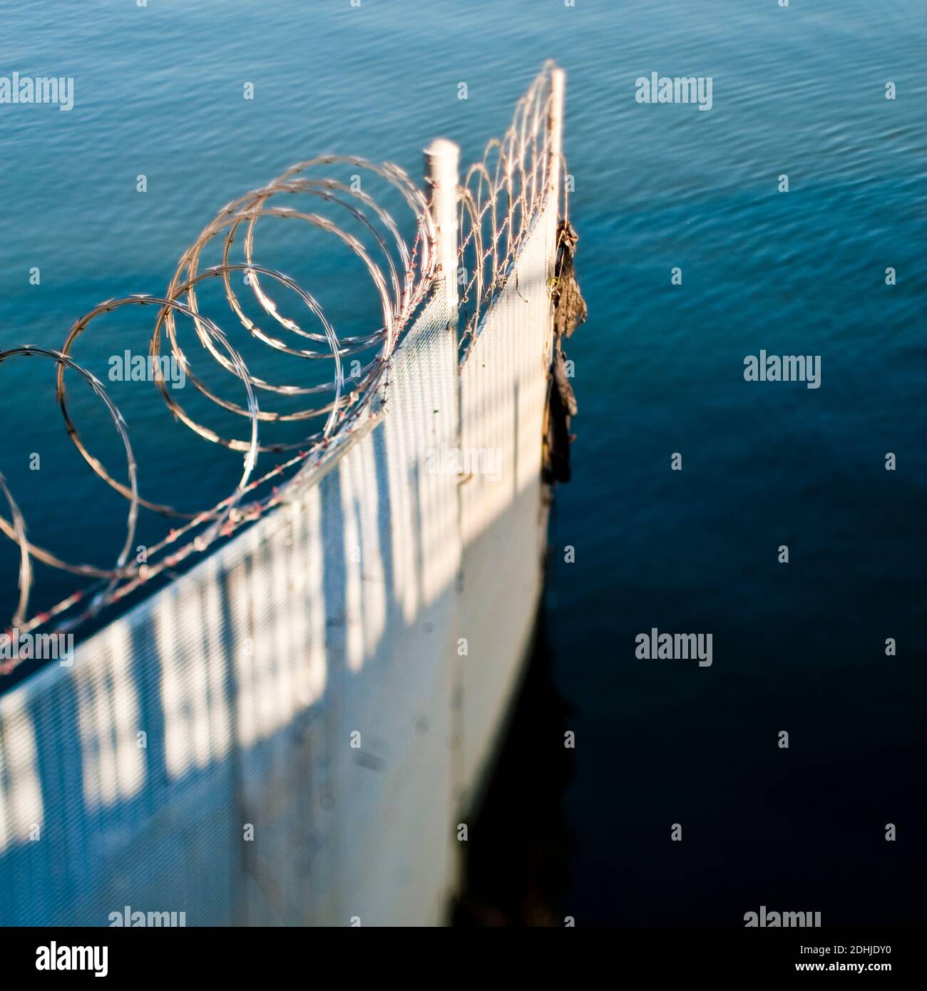 Corrugated iron fence and barbed wire in ocean. Stock Photo