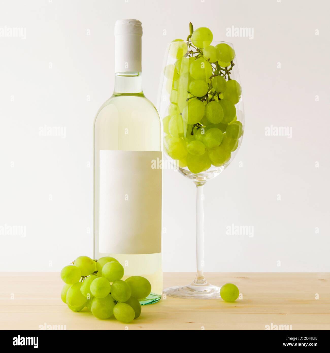 Bottle of white wine with anonymous label and a large and transparent glass goblet filled with grapes Stock Photo